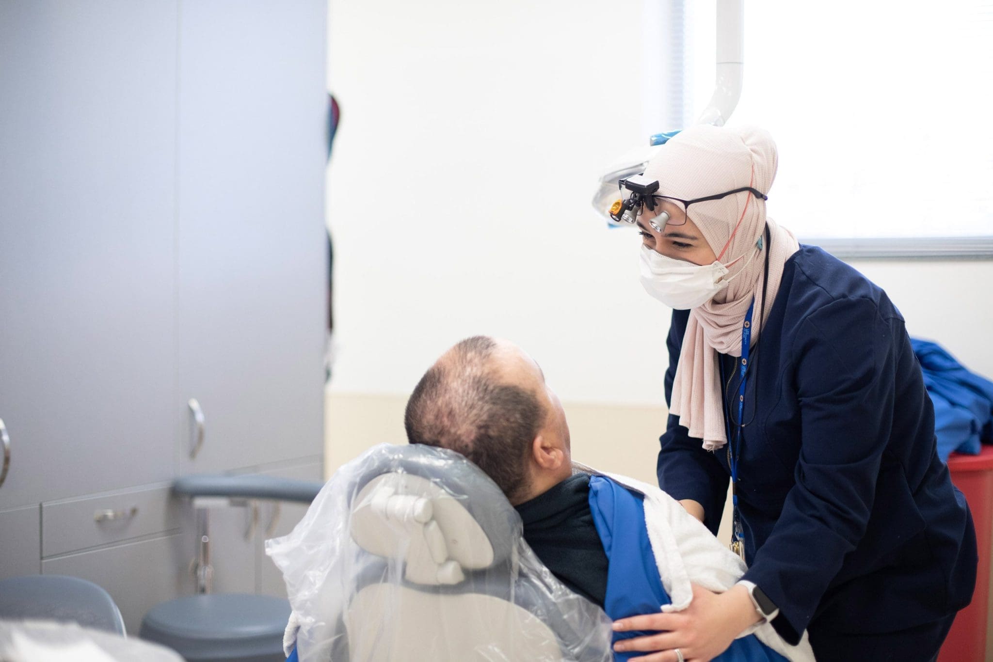Compassionate dentist in hijab provides sensory-friendly care, comforting an autistic patient during a specialized dental appointment for individuals with intellectual and developmental disabilities (IDD).