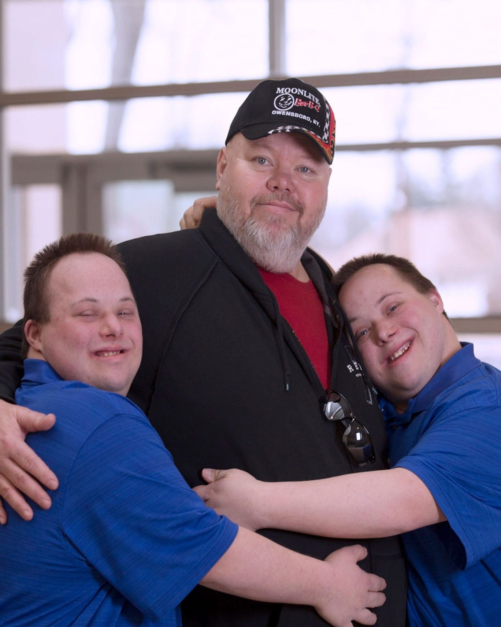 A father smiles warmly as his twin sons, who have Down syndrome, embrace him.